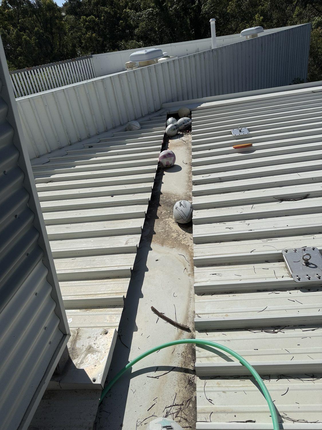 Box gutter on a school roof full of debris with sports balls caught in it