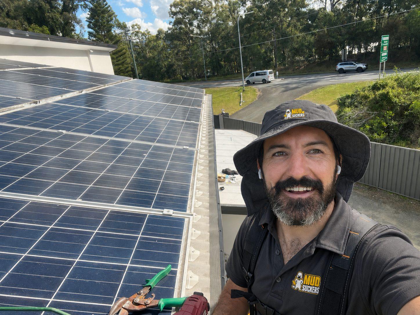 MUDSUCKERS operator in the black branded uniform beside solar panels on a roof